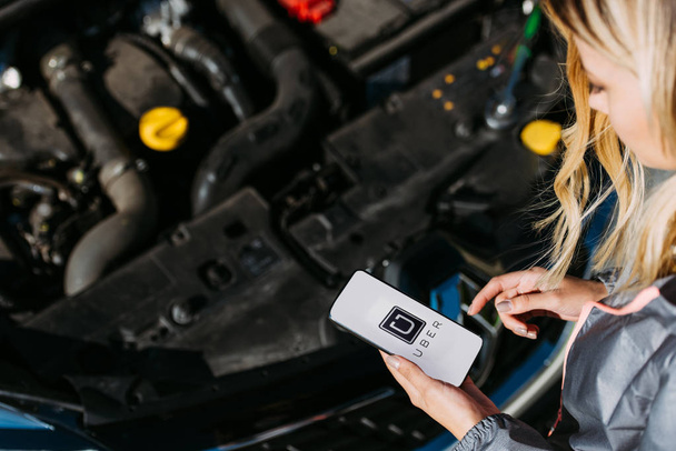 cropped shot of girl using smartphone with uber app while fixing broken car  - Foto, imagen