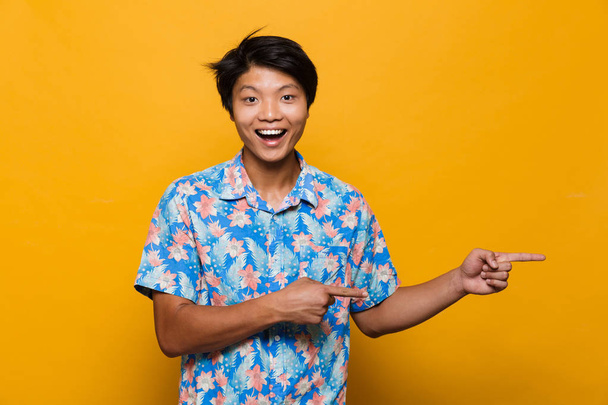 Image of an excited young asian man posing isolated over yellow background pointing. - Valokuva, kuva