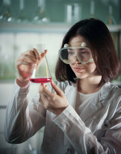 Laboratorium chemiczne. Młoda kobieta w pracy okulary patrząc na kolby - Zdjęcie, obraz