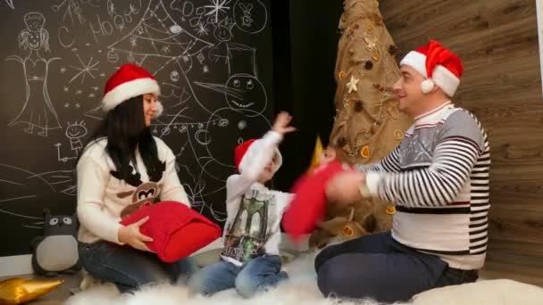 familie zit op een bont beddengoed en wordt gespeeld met kussens in santa hoeden - Video