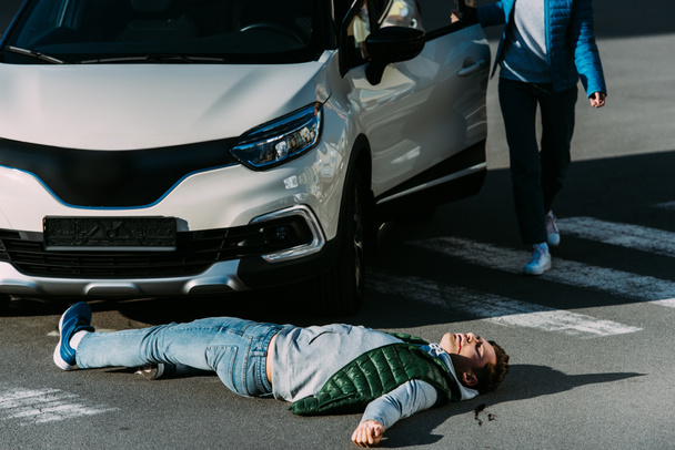 車のドアの開閉しようとして負傷した男の車の事故の後道路に横たわっている女性のクロップ撮影  - 写真・画像