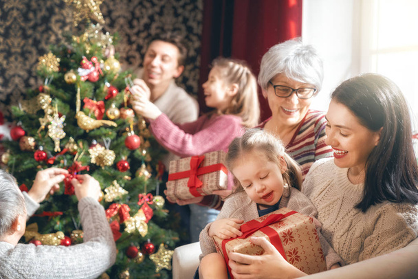 Merry Christmas and Happy Holidays! Grandma, grandpa, mum, dad and child exchanging gifts. Parents and daughter having fun near tree indoors. Loving family with presents in room. - Foto, imagen