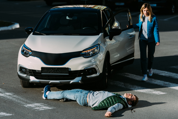 молодая женщина, открывающая дверь машины и идущая к раненому человеку, лежащему на дороге после автомобильной аварии
   - Фото, изображение