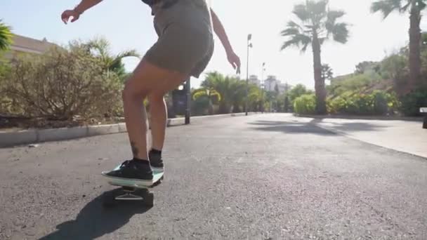 Mädchen auf Skateboard in kurzen Hosen fährt auf der Straße am Strand und unter Palmen entlang - Filmmaterial, Video