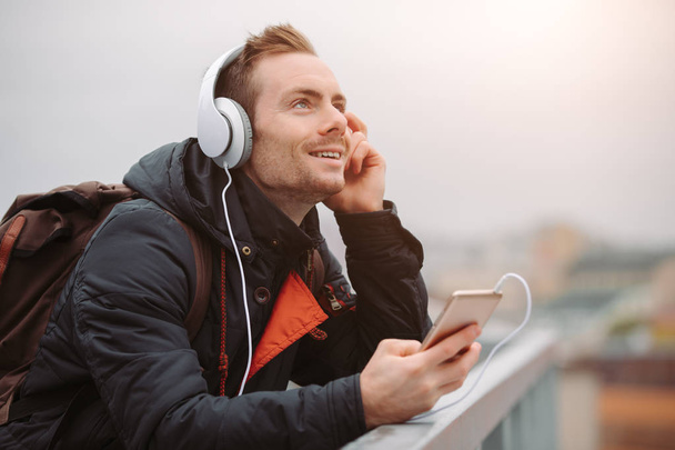 Smiling man in headphones enjoy listening to music outdoors in city rooftop - Photo, image