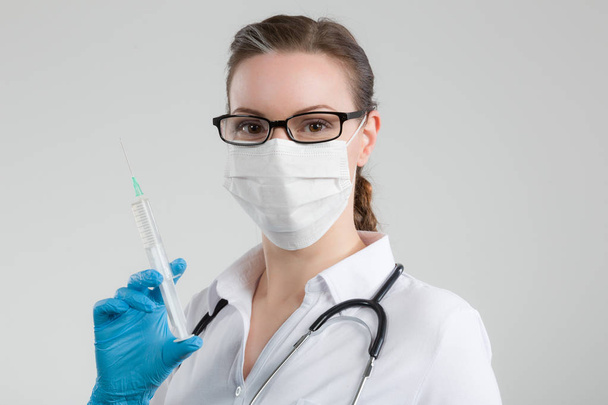 жінка-лікар з шприцом у руці та стетоскопом та медичною маскою для обличчя
 - Фото, зображення