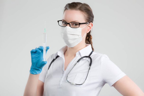врач-женщина со шприцем в руке и стетоскопом и медицинской маской для лица
 - Фото, изображение