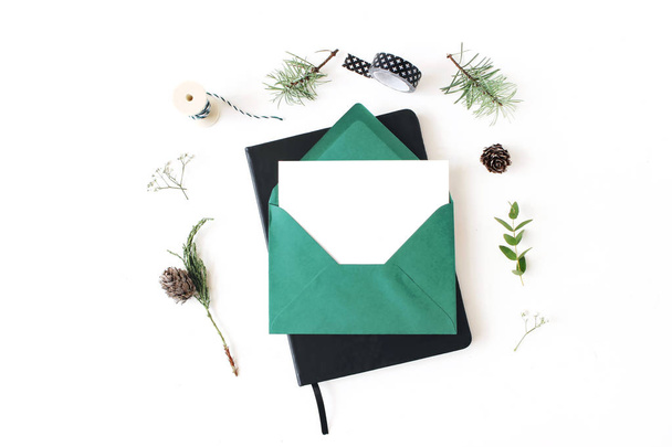Christmas composition. Greeting card, envelope and note pad mock-up scene. Frame of pine, eucalyptus and juniperus tree branches, pine cones and baby breath flowers. White table background. Flat lay. - Photo, Image