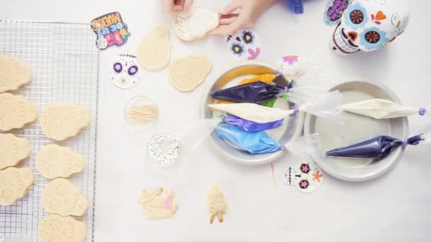 Vista superior das mãos de mãe e filha decorando biscoitos de crânio de açúcar com gelo real para o feriado Dia de los Muertos
. - Filmagem, Vídeo