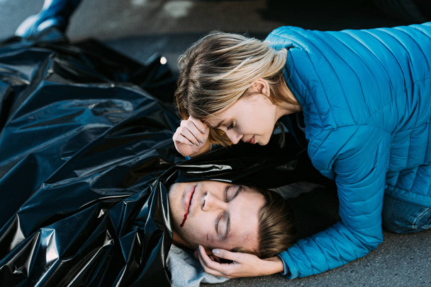 young woman crying and looking at dead man on road  - Photo, image