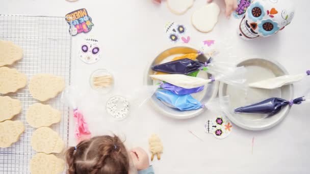 Vue du dessus des mains de la mère et de la fille décorant des biscuits au crâne de sucre avec glaçage royal pour les vacances à Dia de los Muertos
. - Séquence, vidéo