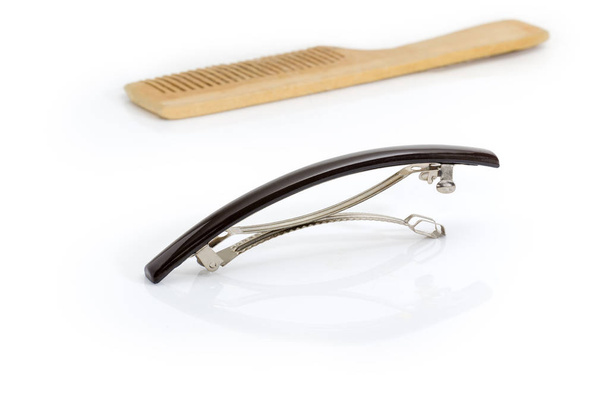 Moderní kovové francouzský sponka vlasů klip s černou plastovou krycí desku na selektivní fokus na rozostřeného pozadí dřevěný hřeben na bílém pozadí - Fotografie, Obrázek