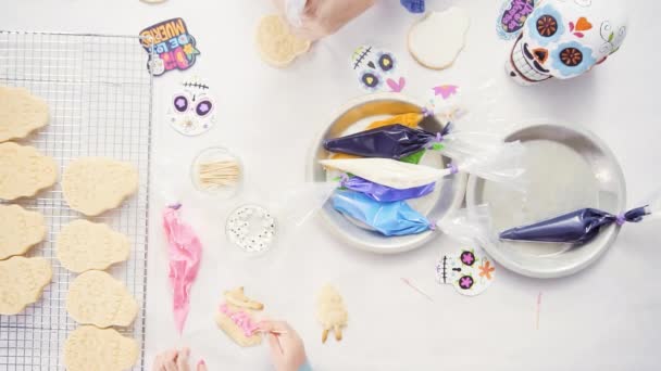 Vue du dessus des mains de la mère et de la fille décorant des biscuits au crâne de sucre avec glaçage royal pour les vacances à Dia de los Muertos
. - Séquence, vidéo
