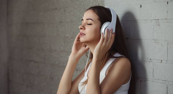 Young woman listening to music with headphones near wall - Φωτογραφία, εικόνα