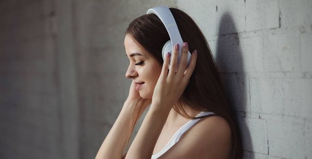 Young woman listening to music with headphones near wall - Foto, afbeelding