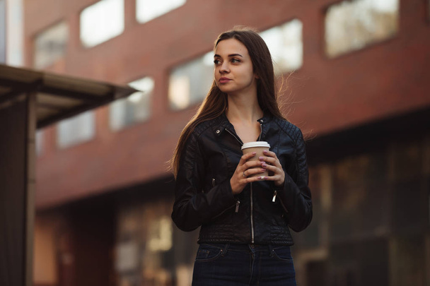Beautiful woman holding paper coffee cup and enjoying a walk in the city - Photo, image