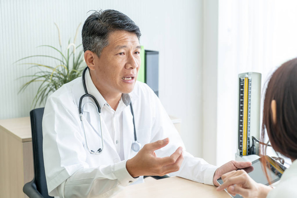 Asian senior doctor and patient are discussing something while sitting at the table - Foto, imagen