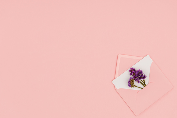 top view of open pink envelope with white card and small purple flowers isolated on pink background  - Photo, Image