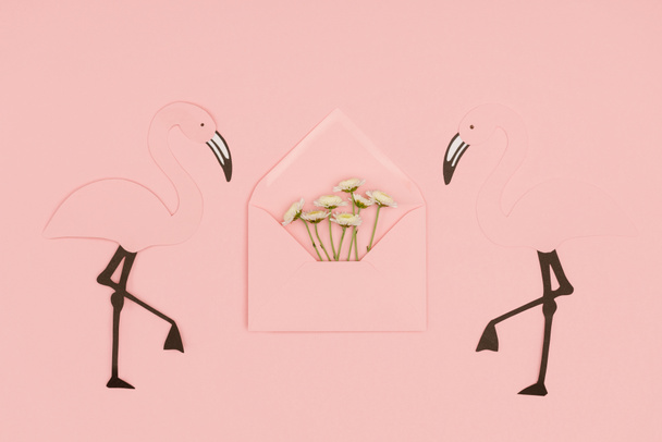 Nahaufnahme eines offenen rosa Briefumschlags mit kleinen weißen Blüten und papiergeschnittenen Flamingos isoliert auf rosa - Foto, Bild