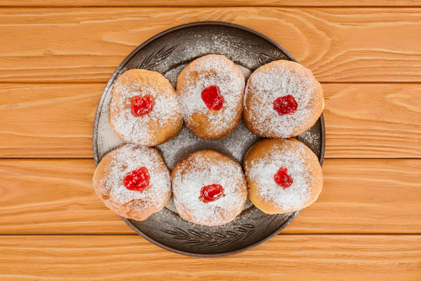 top view of sweet donuts on plate on wooden tabletop, hannukah celebration concept - Фото, изображение