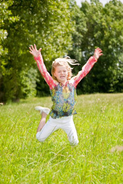 Child of 5 years old jumping high in the field arms outstretched - 写真・画像