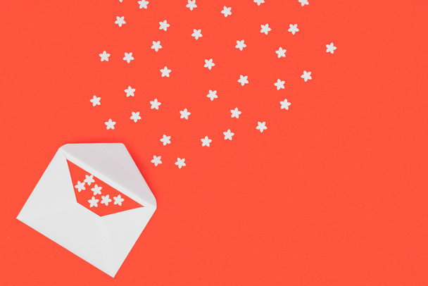 Draufsicht auf offenen weißen Umschlag mit roter Karte und kleinen weißen Sternen auf rotem Hintergrund - Foto, Bild