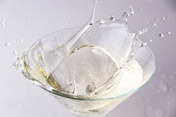 A glass with vermouth and a piece of ice thrown at it. splash and splash of drink - Photo, image