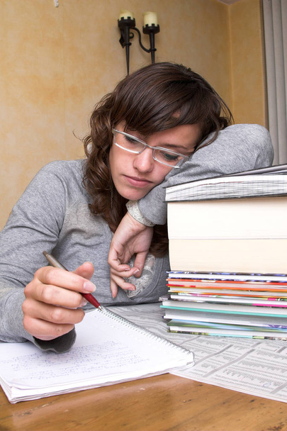 Tired student leaning over her books still looking at her notes - Фото, изображение