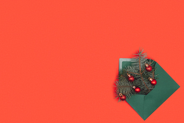 πράσινο φάκελος με κλαδιά έλατου και λαμπερά Χριστούγεννα στολίδια, απομονώνονται σε κόκκινο  - Φωτογραφία, εικόνα