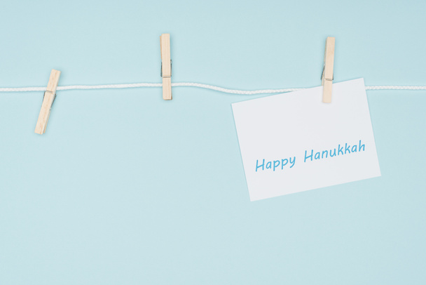top view of happy hannukah card pegged on rope with clothes peg isolated on blue, hannukah concept - Foto, immagini