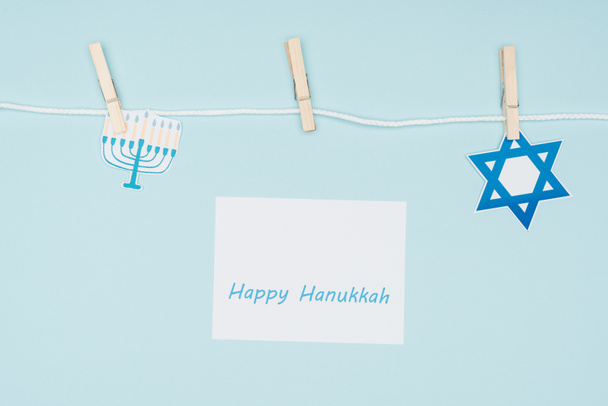 top view of happy hannukah card and holiday paper signs pegged on rope isolated on blue, hannukah concept - Photo, Image