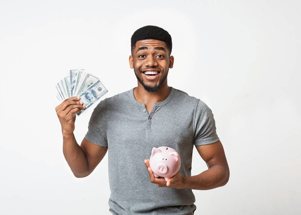 negro hombre celebración dinero y piggybank en blanco fondo
 - Foto, Imagen