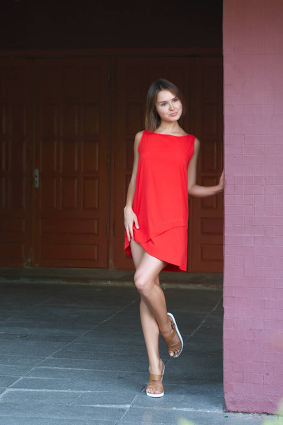 Full length portrait of cute girl in short red dress near brick wall.  - Zdjęcie, obraz