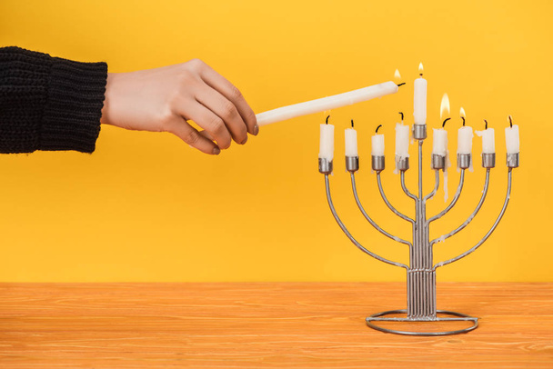 partial view of woman lighting candles on menorah isolated on yellow, hannukah holiday concept - Fotó, kép