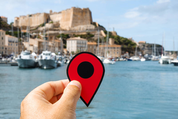 Nahaufnahme der Hand eines kaukasischen Mannes mit einem roten Marker am Hafen von Bonifacio, in corse, Frankreich, und seiner berühmten Zitadelle im Hintergrund - Foto, Bild