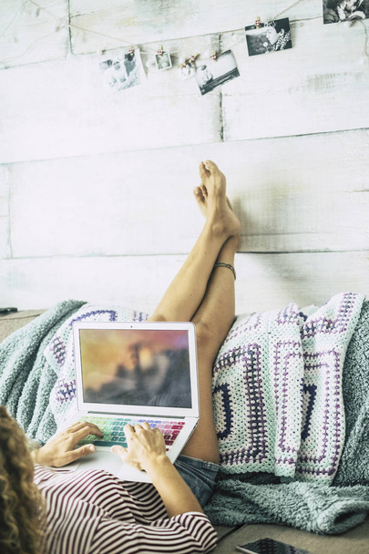 女性はソファの上で横になり、足は壁の上で休んでいますリラックスしてコンピュータを見て - 写真・画像