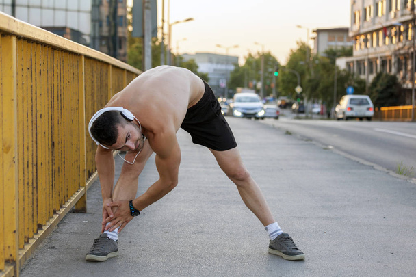 Male runner doing stretching exercise on the bridge,preparing for morning workout in the park.Fitness and lifestyle concept. - Photo, Image