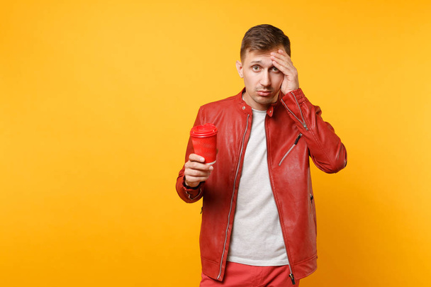 Portrait of vogue young man 25-30 years in red leather jacket, t-shirt with cup coffee isolated on bright trending yellow background. People sincere emotions lifestyle concept. Advertising area. - Photo, Image