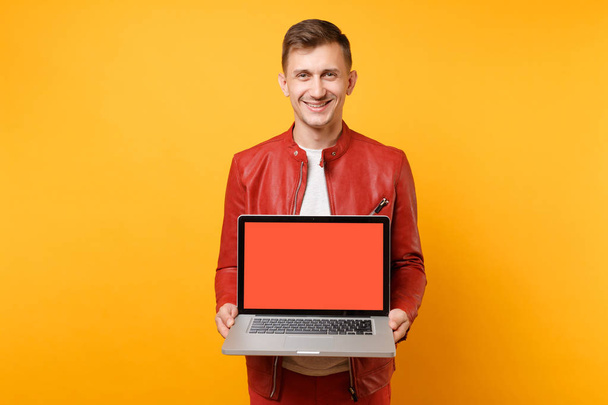 Portrait vogue amusant jeune homme en veste en cuir rouge, t-shirt tenir ordinateur portable écran vide vide isolé sur fond jaune vif. Les gens sincères émotions concept de style de vie. Espace publicitaire
 - Photo, image