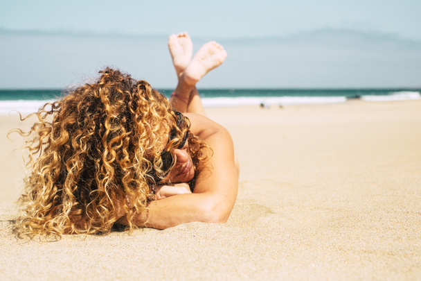 Beautiful tanned lady with curly blonde hair laying at beach at summer  - Valokuva, kuva