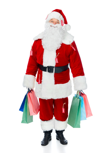 glücklicher Weihnachtsmann in rotem Kostüm mit Verkaufsetiketten, die Einkaufstüten isoliert auf weißem Grund halten - Foto, Bild