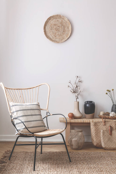 Wicker chair with striped pillow on it next to wooden table full of accessories such as vase, flowers and candles - Foto, afbeelding