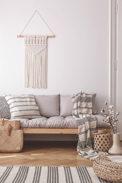 Beige, handmade macrame on a white wall above a couch with a striped linen pillow in a natural living room interior - Photo, Image