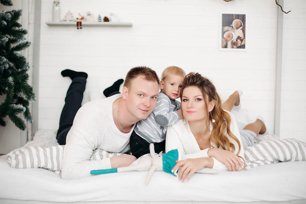 Matka i ojciec z synem Ładna, leżąc na łóżku i patrząc na kamery w studio w zimie - Zdjęcie, obraz