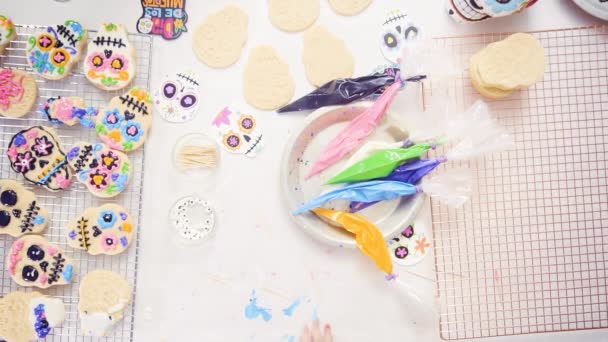 Petite fille décorant des biscuits au crâne de sucre avec glaçage royal pour les vacances à Dia de los Muertos
. - Séquence, vidéo