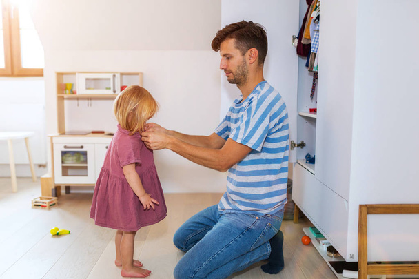 Dad is helping toddler daughter to get dressed - Foto, imagen