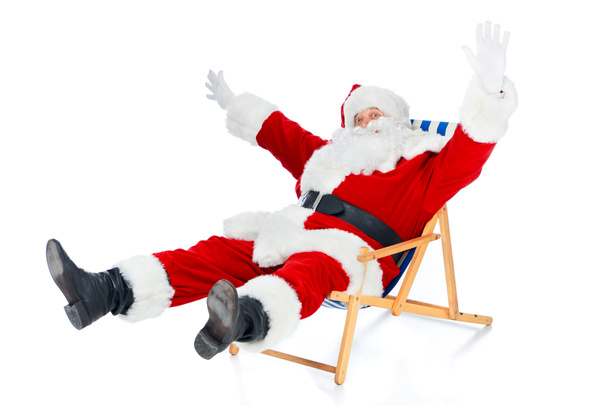 excited santa claus gesturing and sitting on beach chair on white - Photo, Image