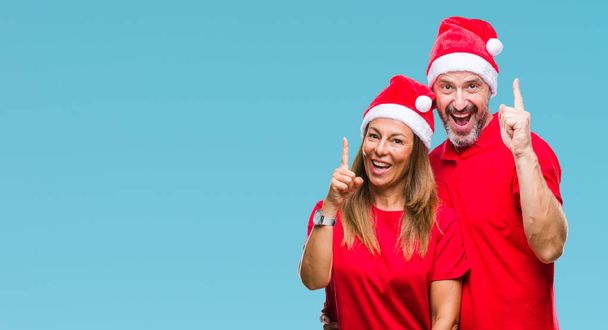 Испанская пара средних лет носит рождественскую шляпу на изолированном фоне, показывая пальцем на успешную идею. Взволнован и счастлив. Номер один
. - Фото, изображение