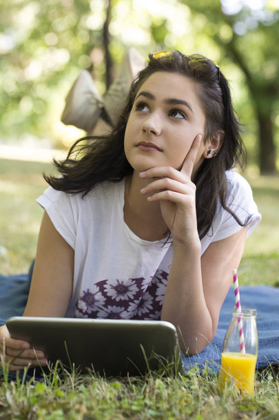 Piękna młoda dziewczyna nastoletnich leżąc na trawie i przy użyciu tabletu. Ona lubi piękny słoneczny letni dzień. Relaks, pobyt w przyrodzie - Zdjęcie, obraz