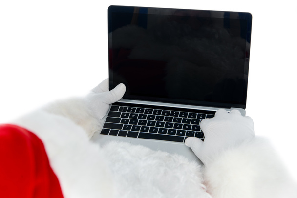 partial view of santa claus using laptop with blank screen isolated on white - Foto, afbeelding